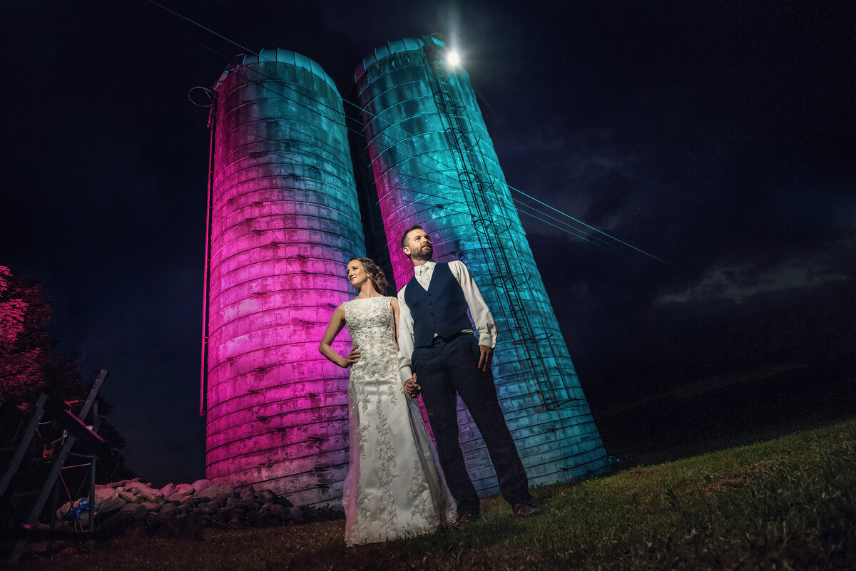 Bride and groom posing for an artistic wedding photo by a rustic barn.