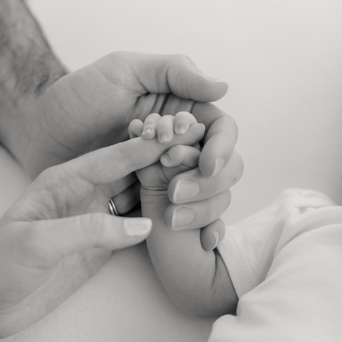 close up of baby holding mom's finger while dad holds baby's hand