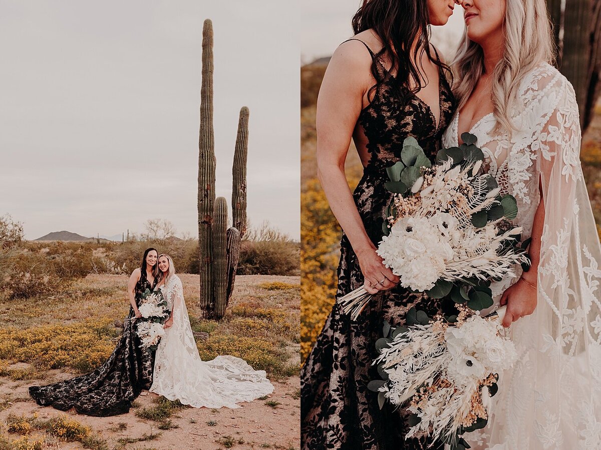 Two brides embrace in the desert, one wearing  a black dress and the second bride wearing a white dress