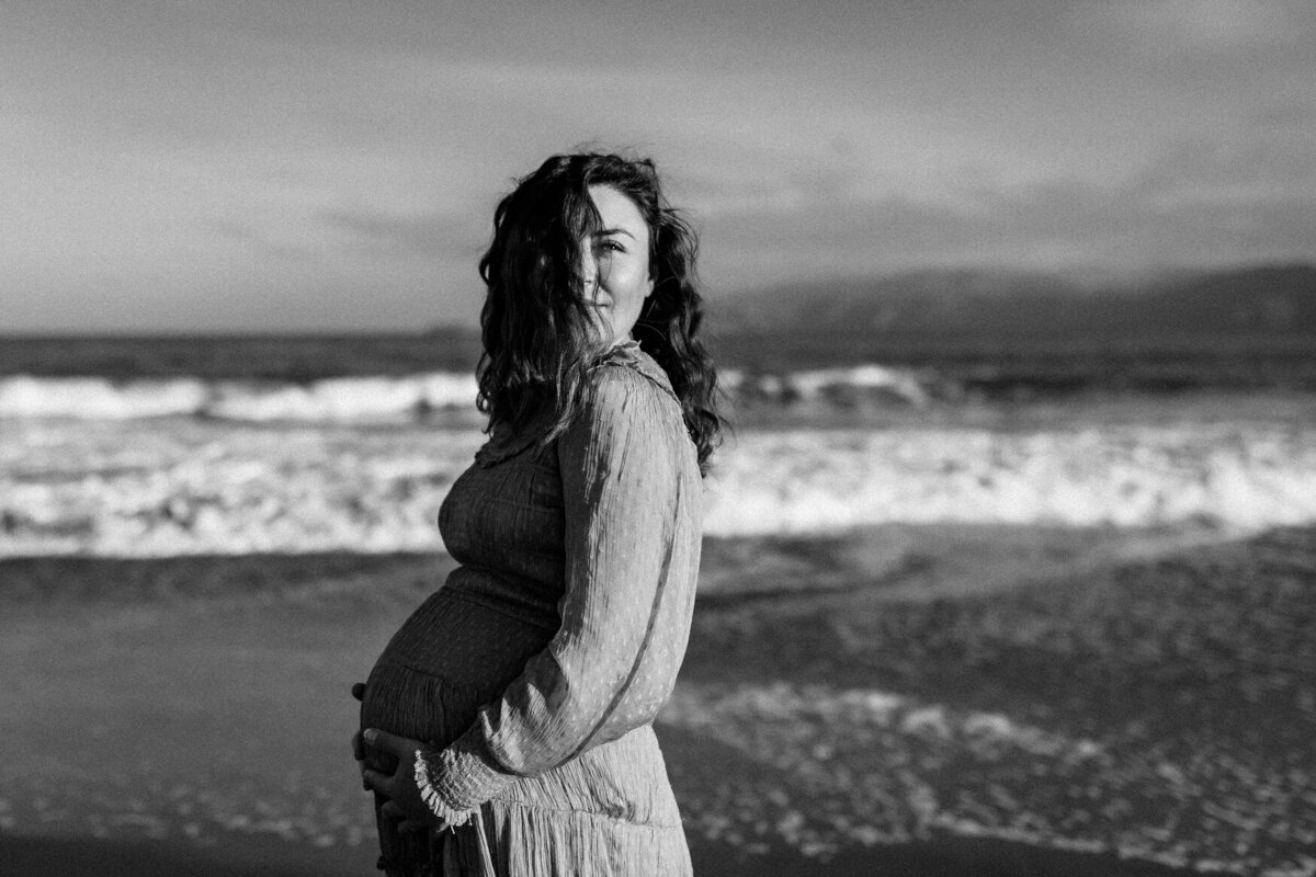 Black and white pregnancy portrait with ocean as backdrop at Baker Beach in San Francisco
