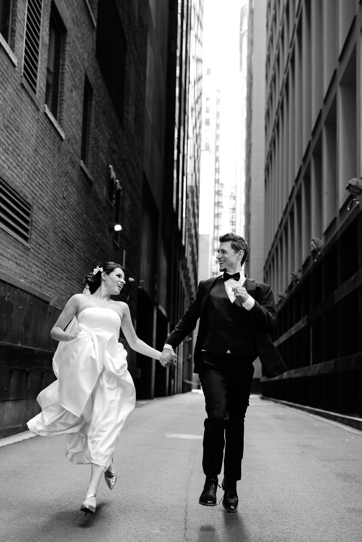 Black and white picture of Bride and Groom holding hands and running in the dark alley of Chicago streets