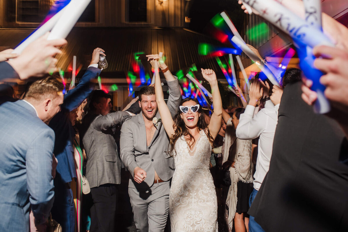 photo of a bride and groom holding hands and running through a tunnel of foam glow sticks