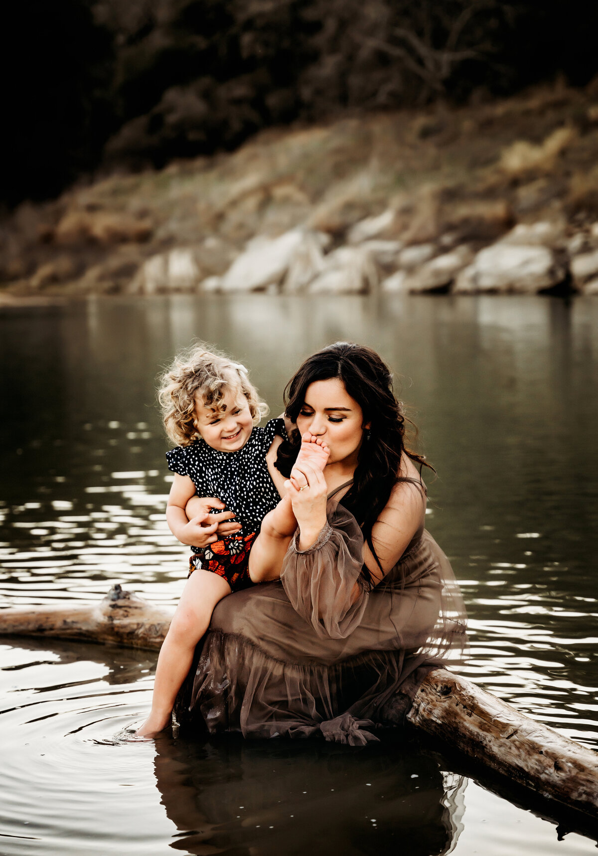 Family Photography, a little girl sits with mom smiling  as mom sits in the lake