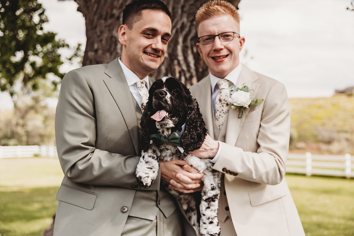 The grooms hold their dog during their mountain-themed wedding at Camelot Ranch in Billings, MT.