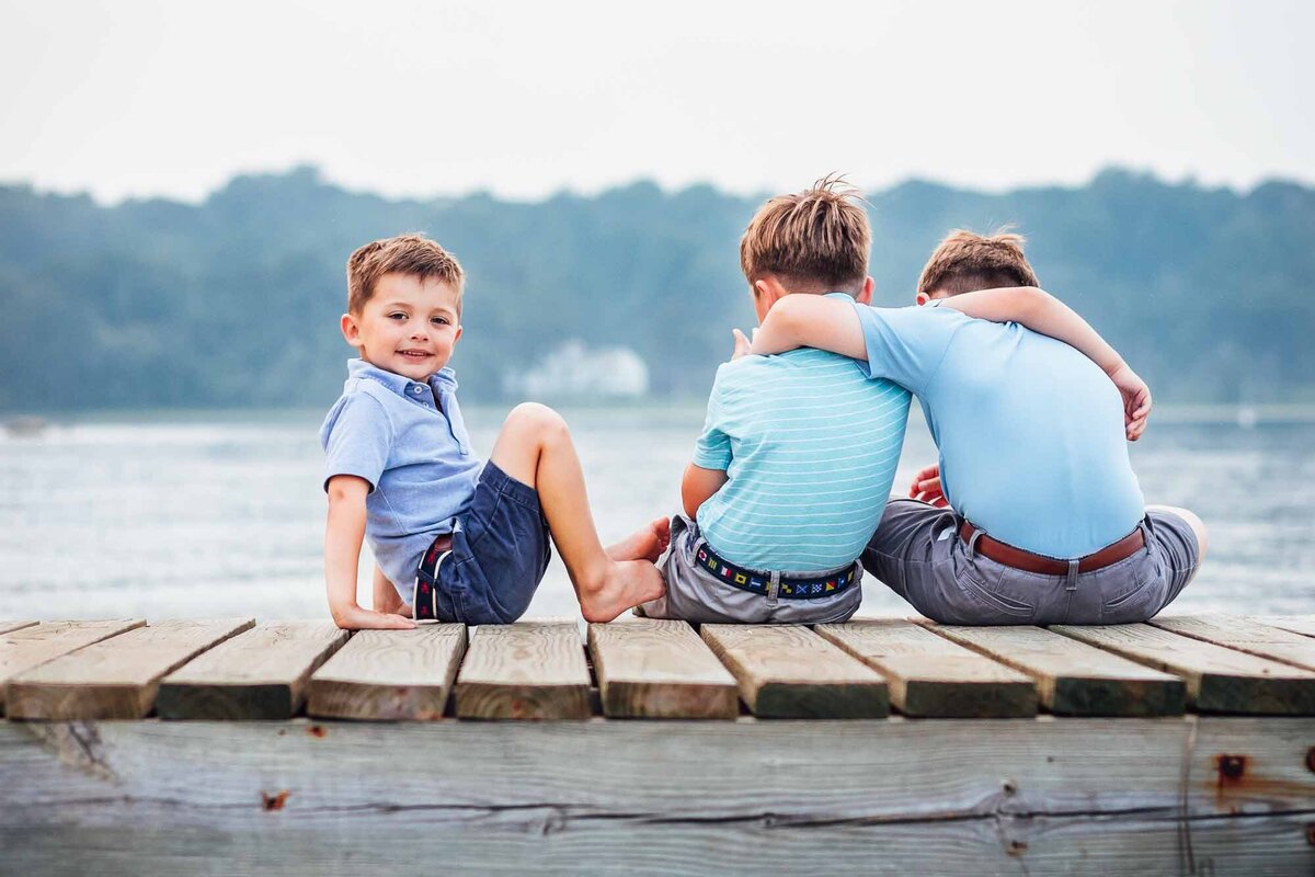 brothers sitting on dock during family photo session on long island beach