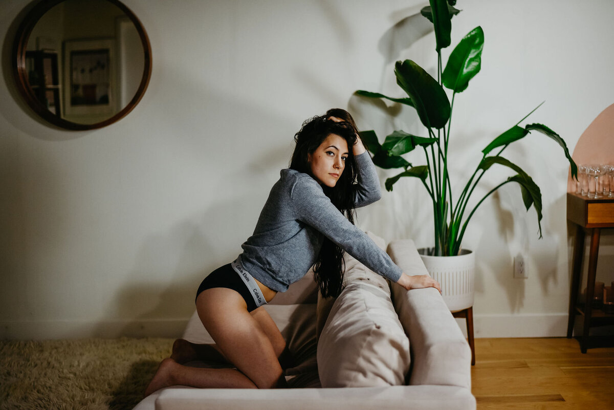 Brunette woman poses on couch in Calvin Klein underwear and gray sweater in Eugene, OR boudoir studio.