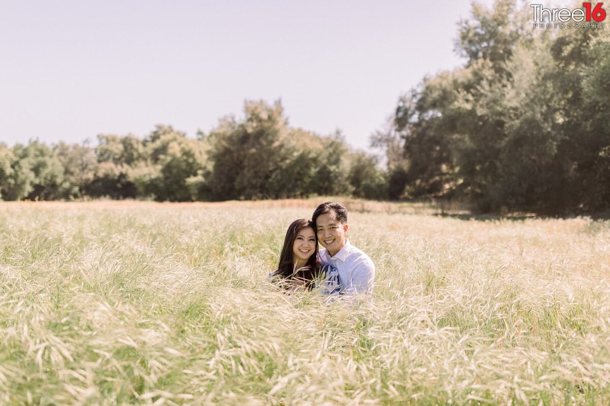 Engaged couple sit together in the middle of a field of tall grass