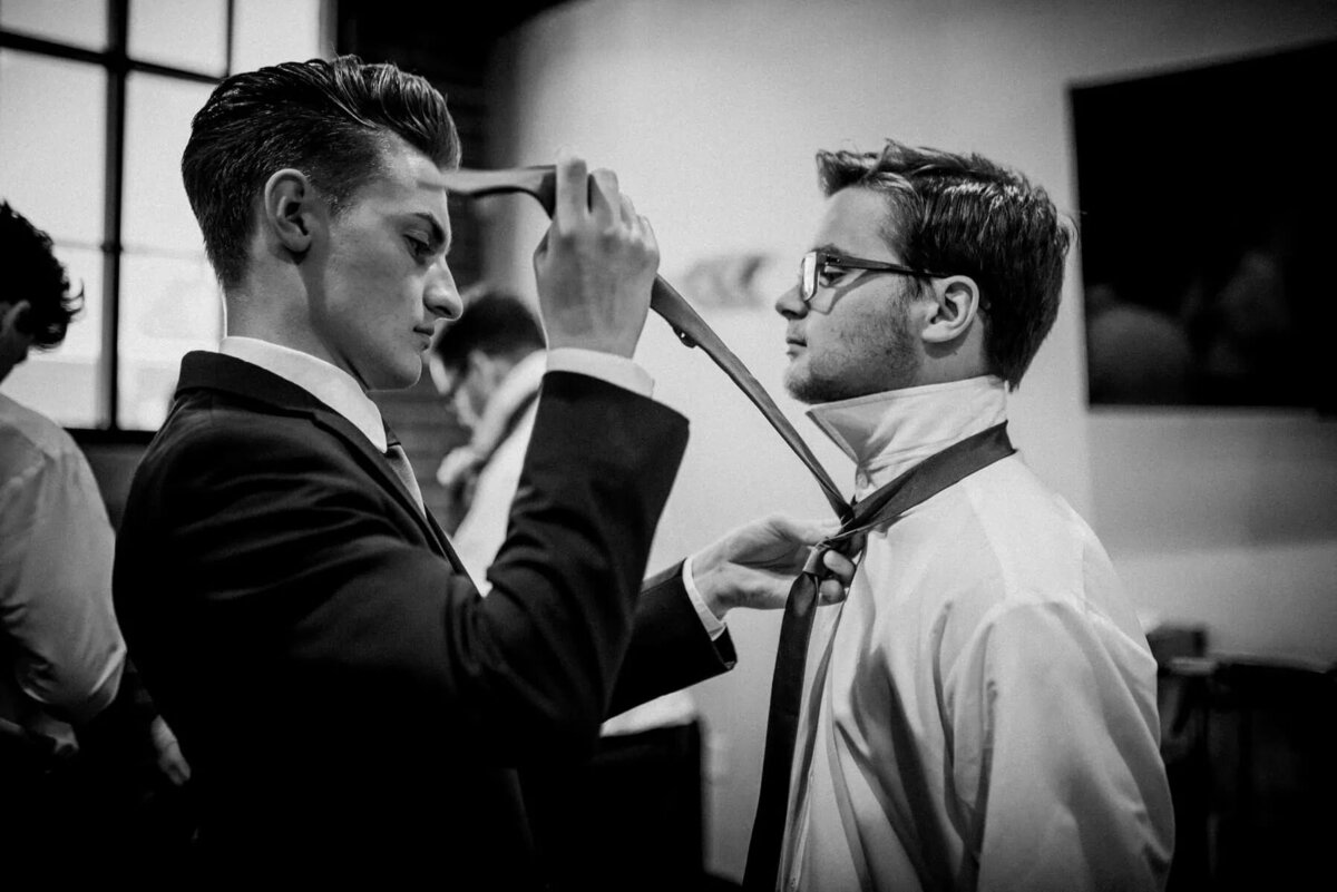 A man helping a groom tie his tie.