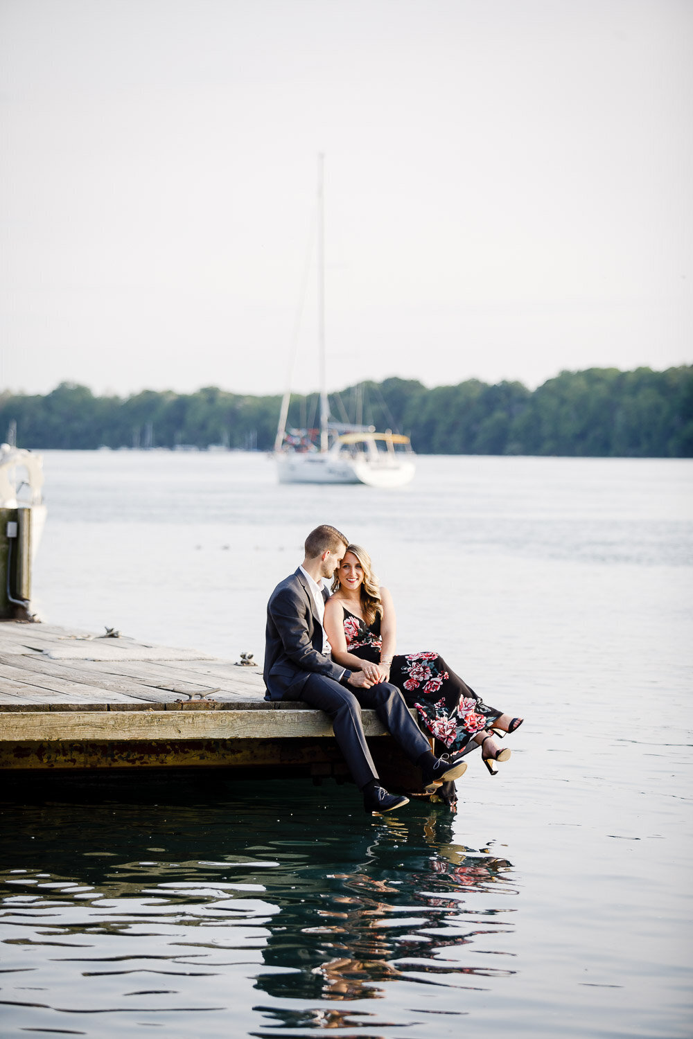 Engaged couple sitting on dock on harbour