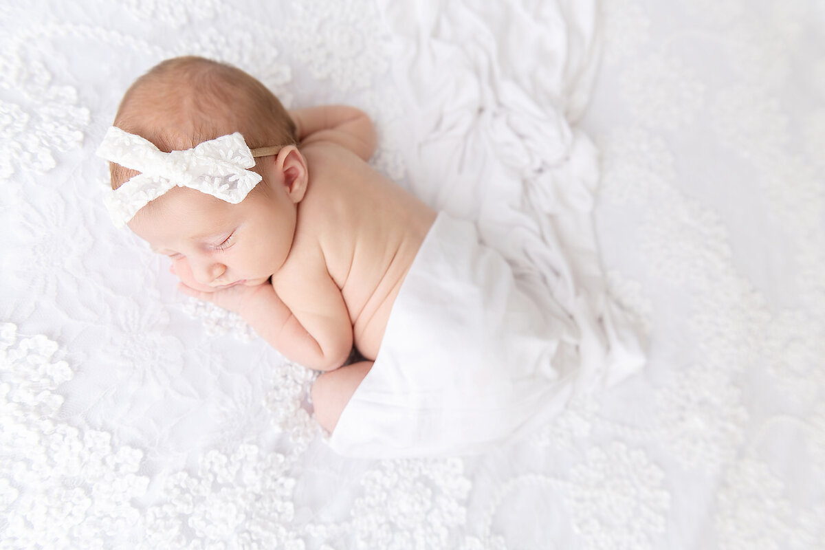 A newborn baby sleeps in an Atlanta newborn photographer studio under a blanket in a white bow