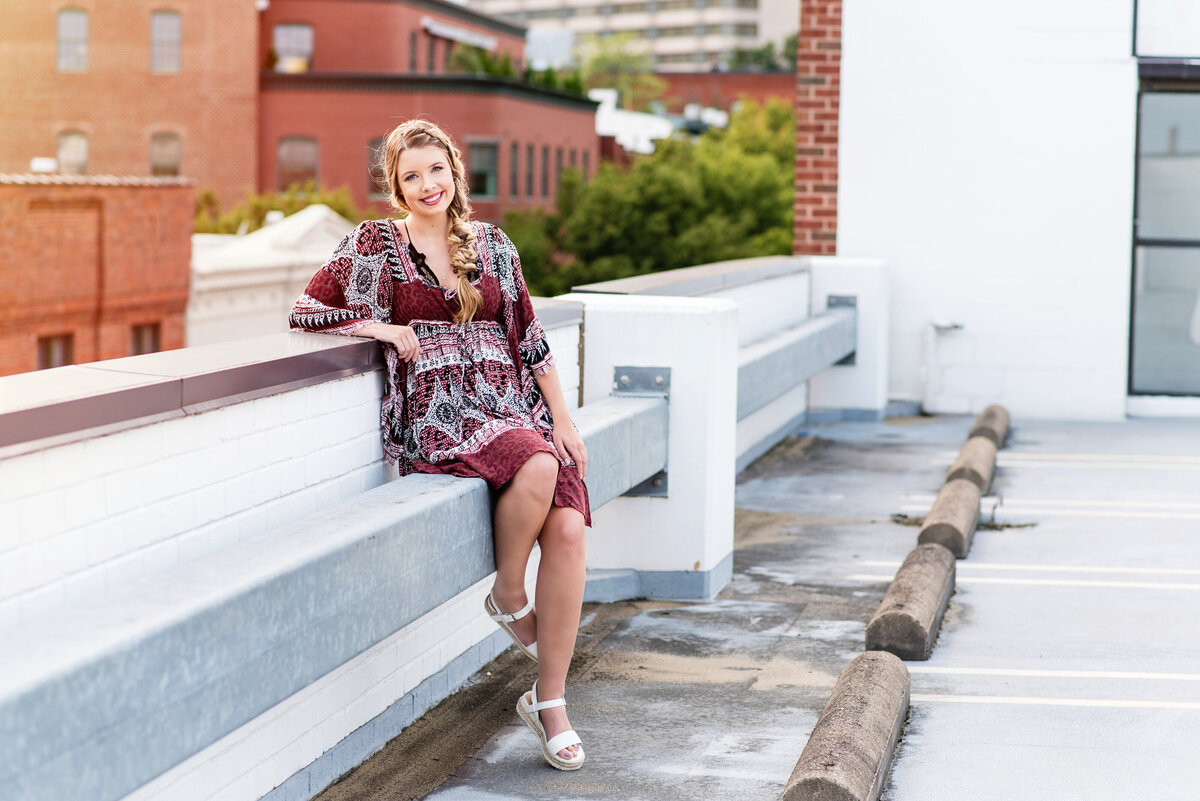 James River high school senior girl sits on rooftop downtown Richmond, VA during sunset during her senior portrait session.