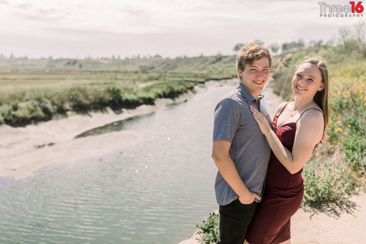 Engaged couple pose together as they smile for the camera next to a creek