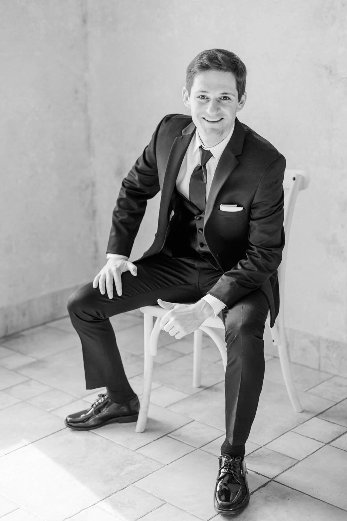 Groom posing for a classic portrait, sitting in a chair in his suit.