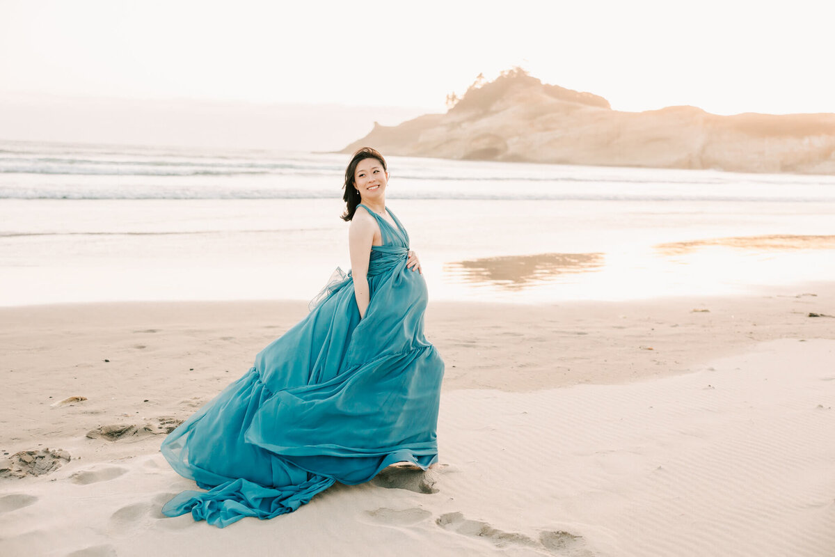 mom with black hair wearing blue flowy dress for maternity portrait on the oregon coast