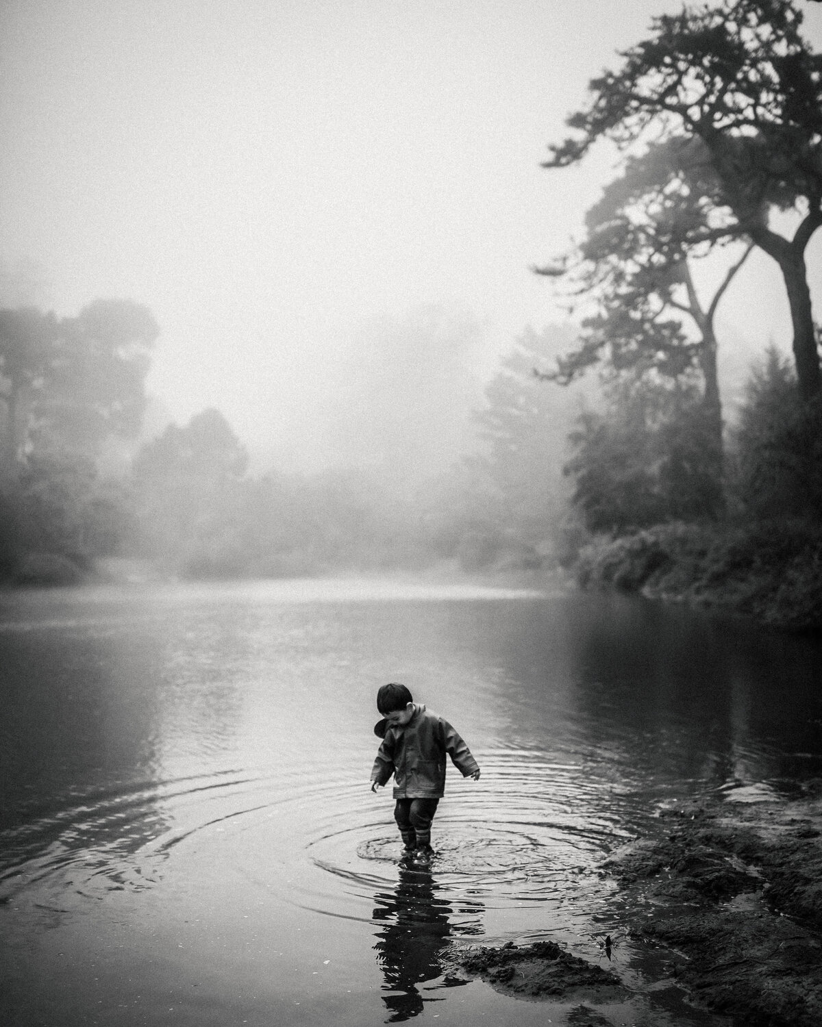 Boy in rain boots walks in lake making ripples on foggy San Franciscan day