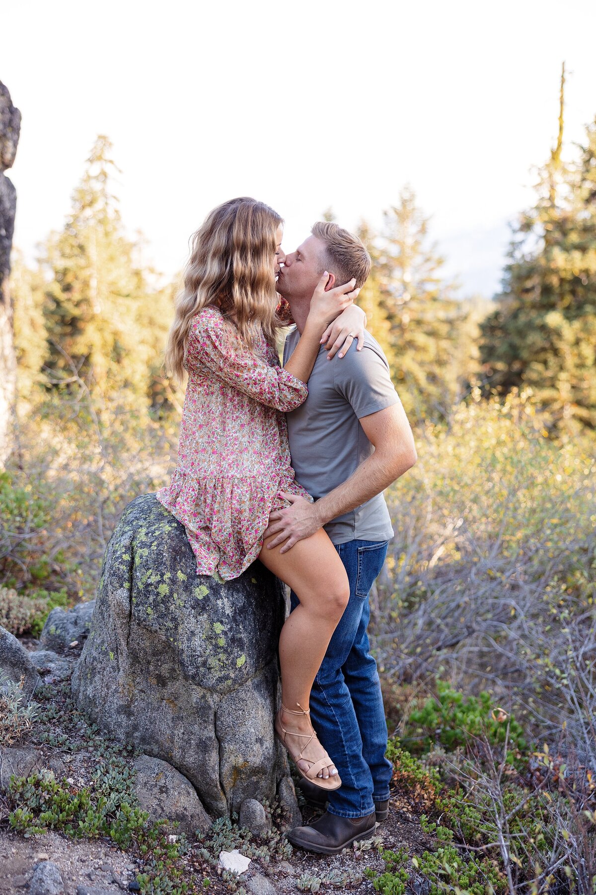 engaged couple kissing on a rock in the forest