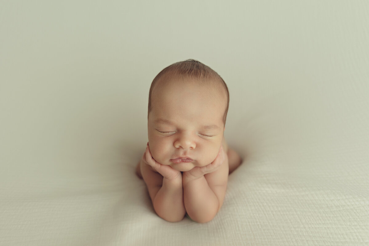 A newborn baby sleeps resting its head on its hands in a studio