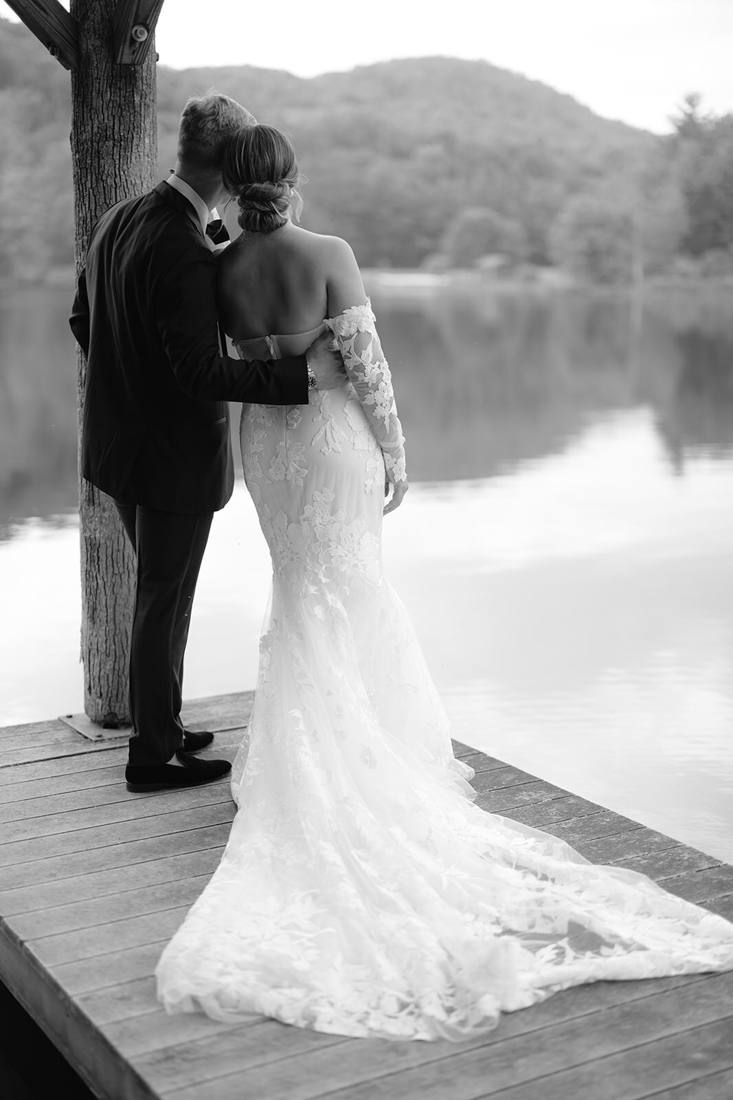 Bride and groom embrace on dock looking out at North Carolina mountains