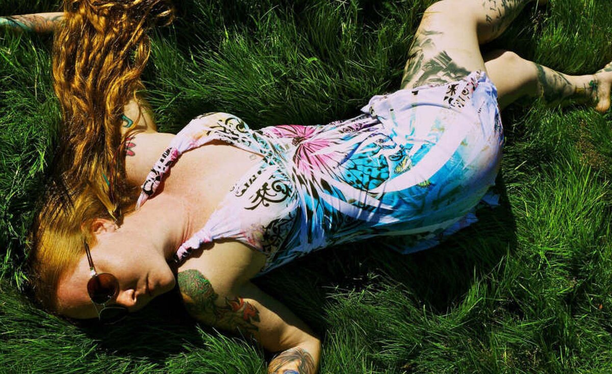 Female musician portrait Layla Zoe wearing sunglasses tie dyed dress lying down  against grass backdrop