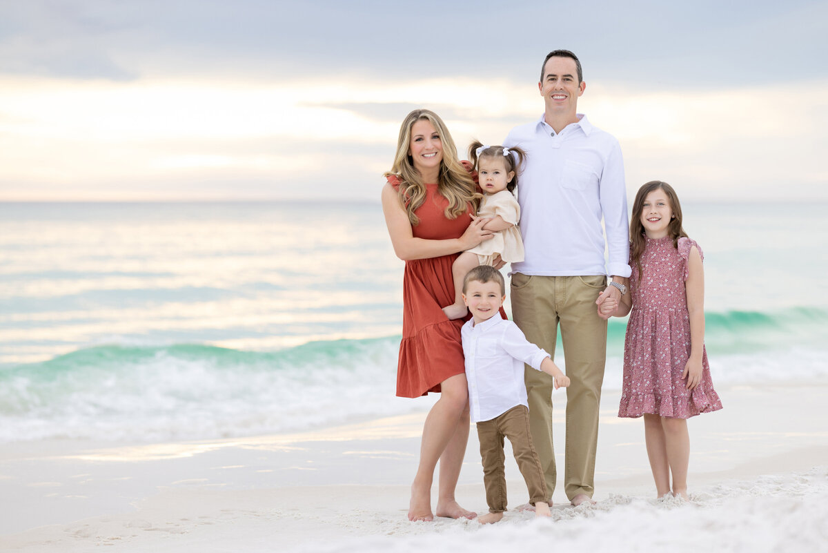 A family of five standing in the sand next to the ocean