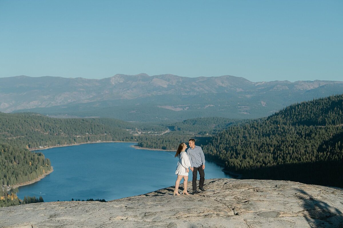 engagement session couple standing on rock donner lake in background. fiance in white dress.