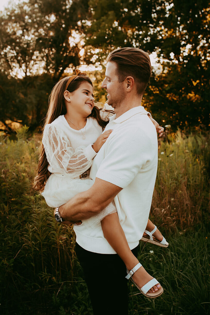 a dad and daughter looking at each other adoringly in a gorgeous field at sunset