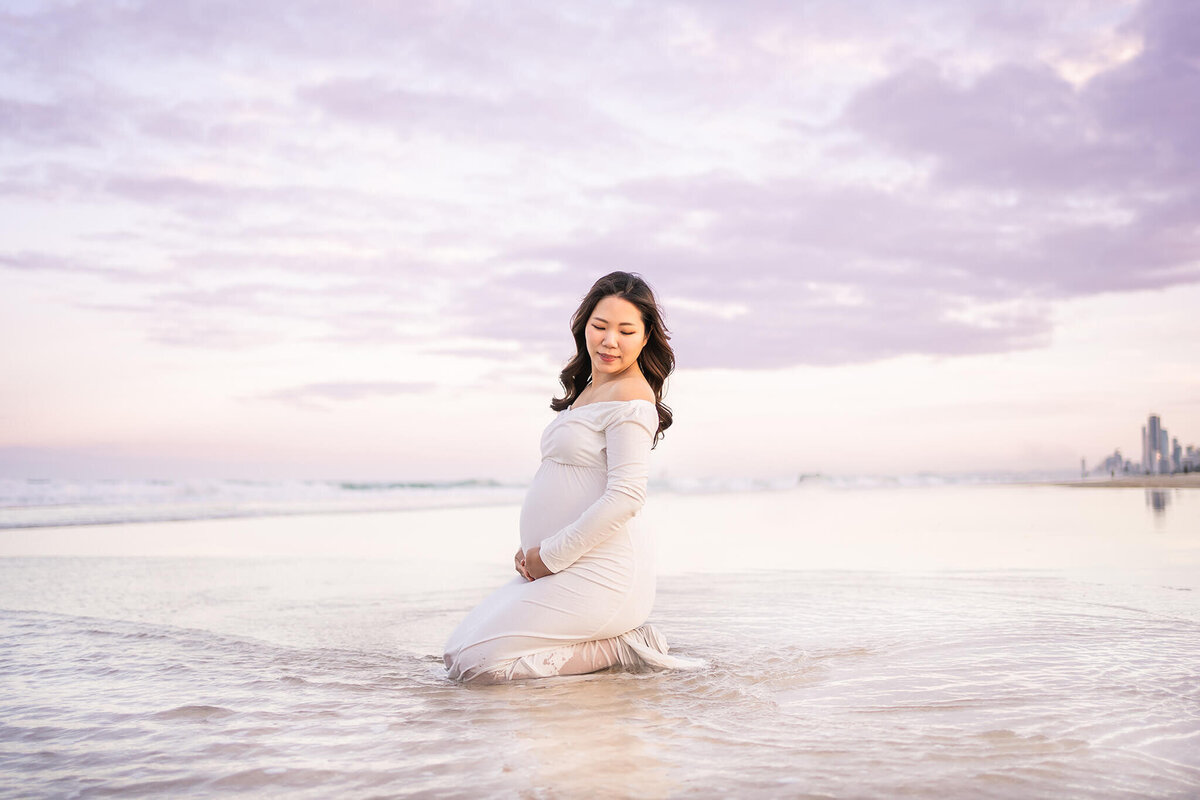 Pregnant woman sitting in water having maternity photoshoot done on Broadbeach Gold Coast QLD