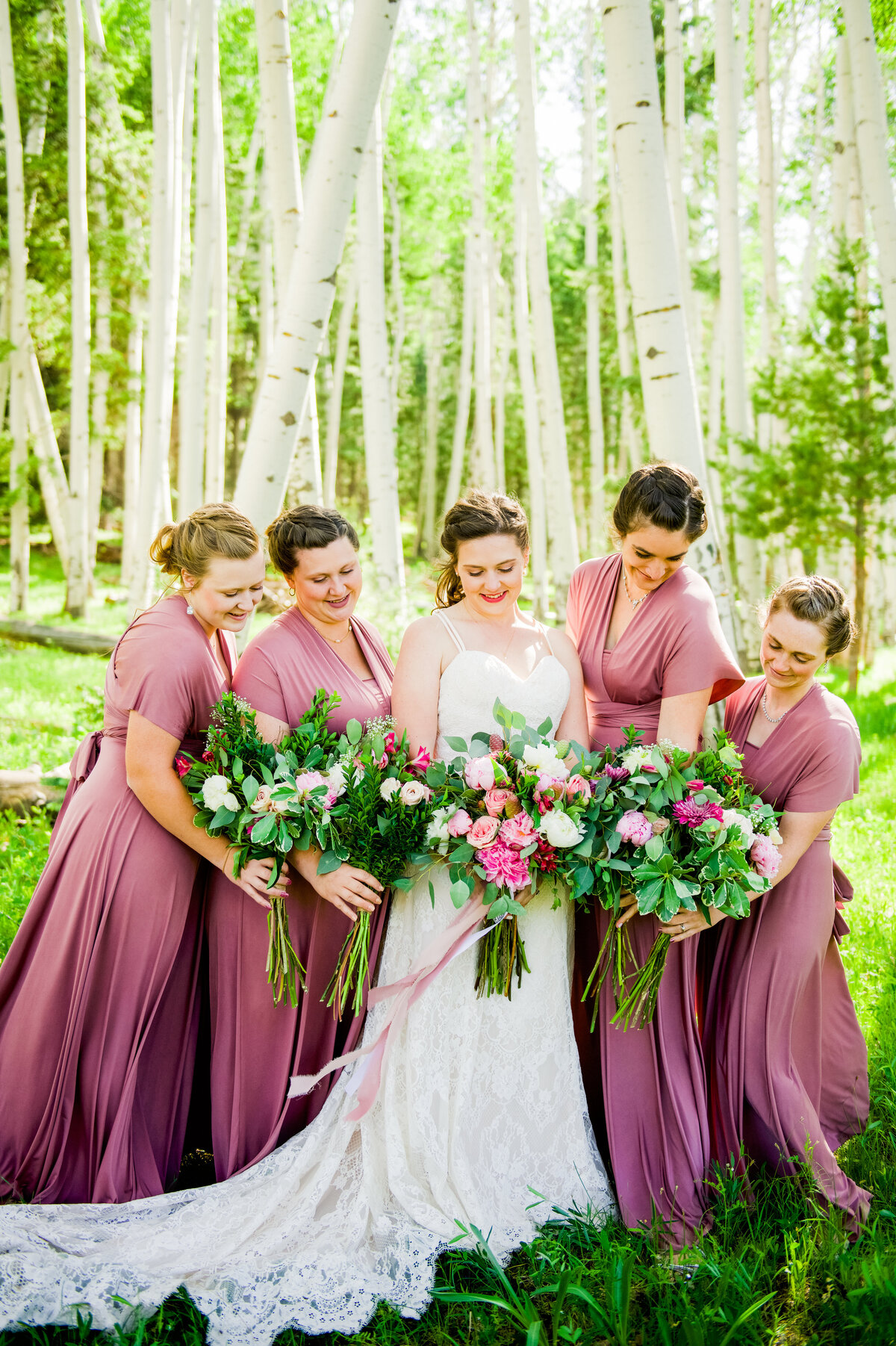 Bride and bridesmaids looking down at bouquets in aspens sun shining Flagstaff summer green