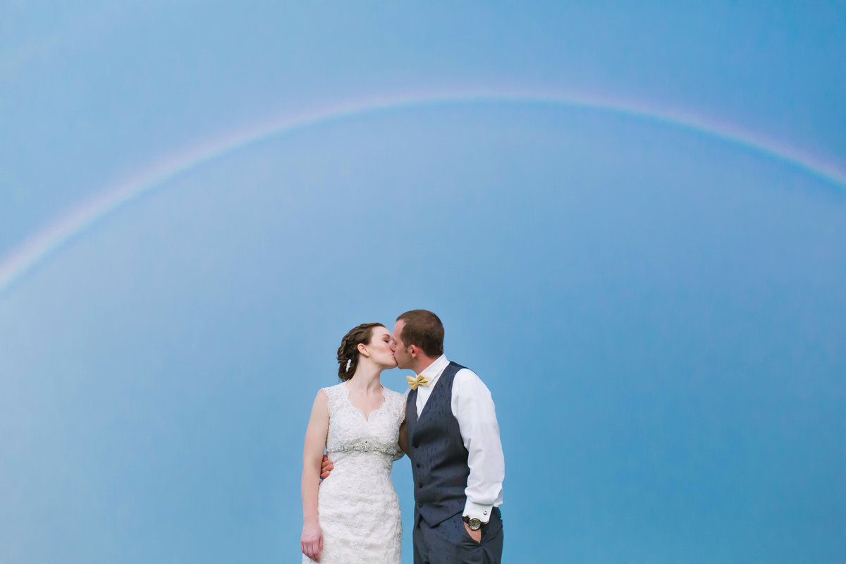 The bride and groom kiss under a rainbow at Veasey Park in Groveland Massachusetts