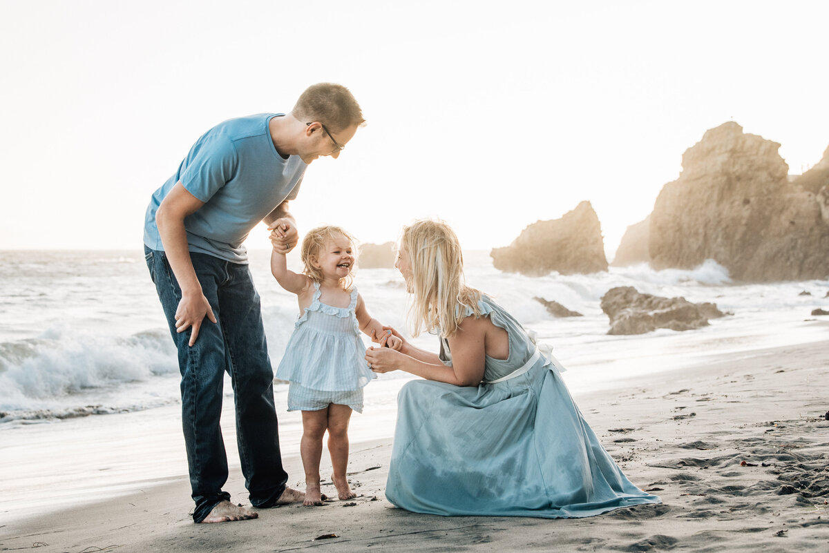 Mom and Dad pose with toddler on Malibu beach at sunset