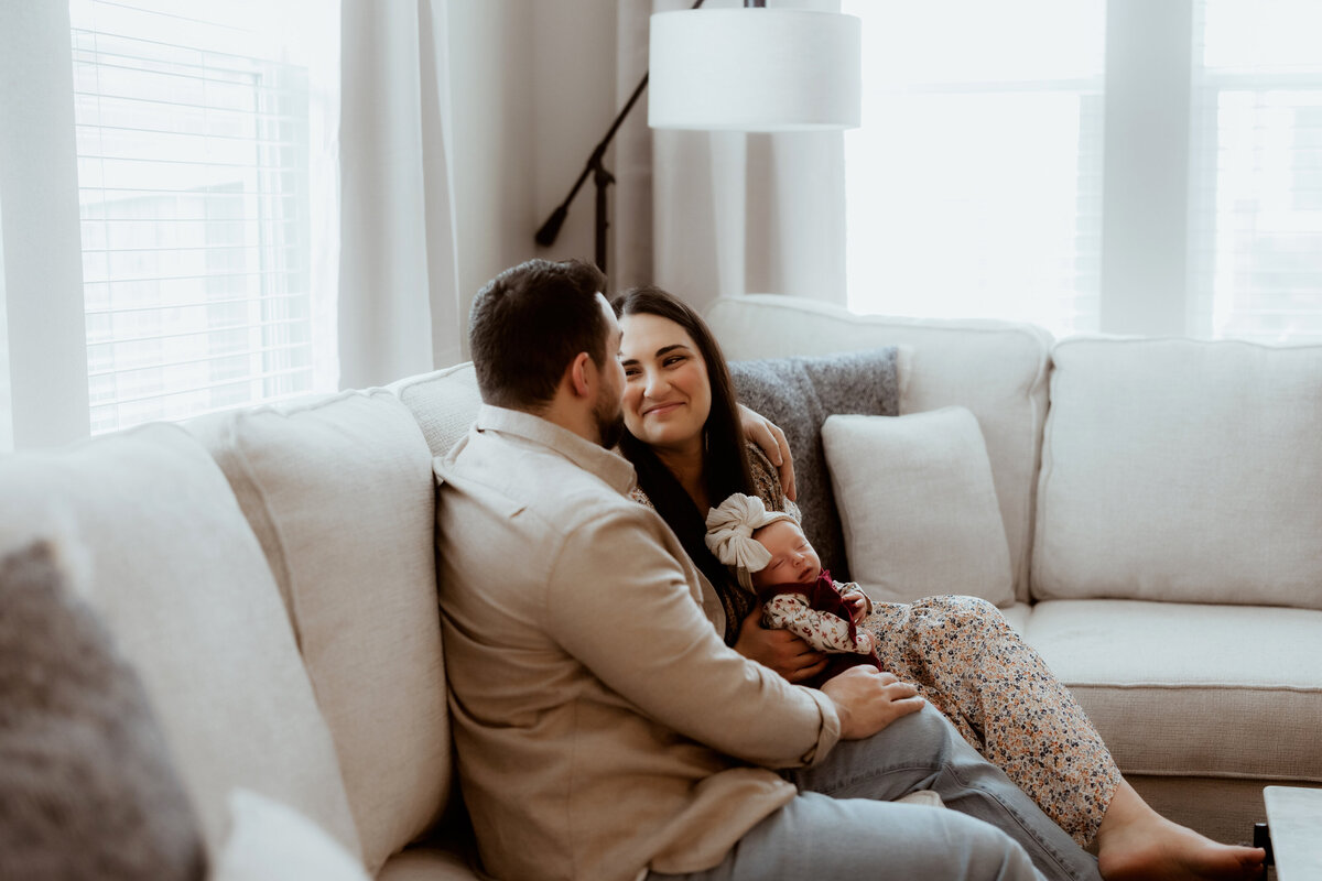 newborn baby girl cuddle with mom and dad in living room for newborn session