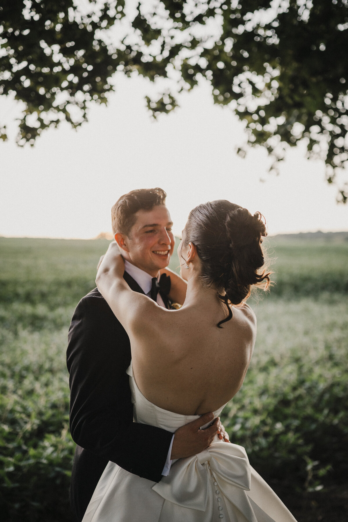 Groom holding bride and looking at her in a field