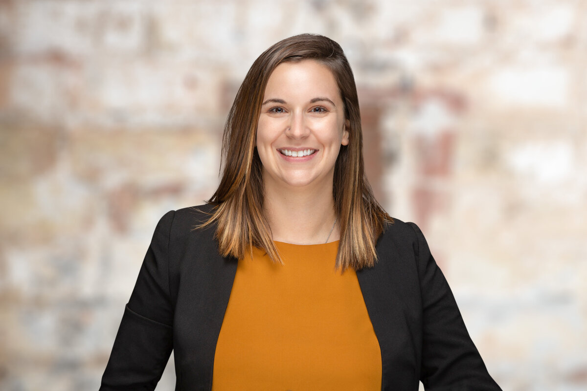 A woman real estate professional poses for a headshot on a brick background at Janel Lee Photography studios in Cincinnati Ohio