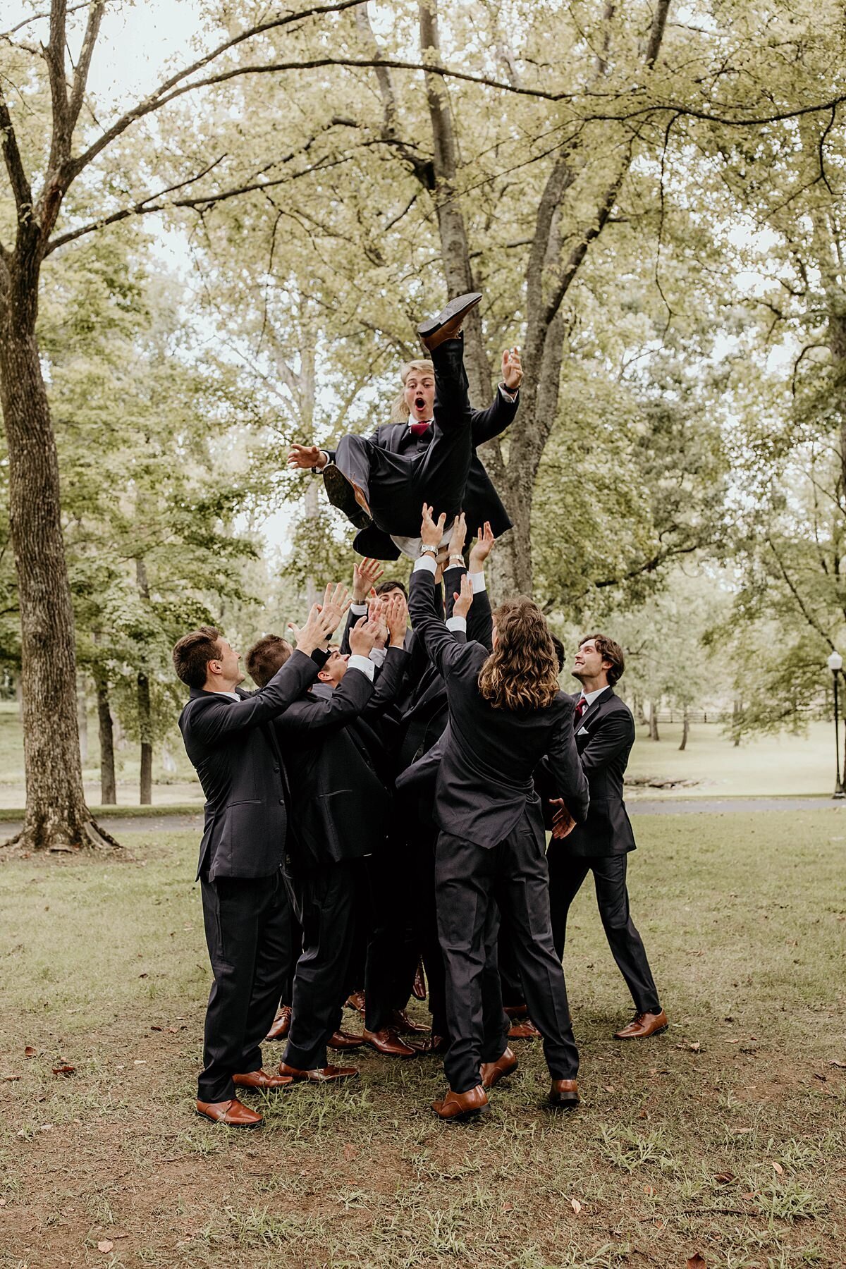 Groomsmen throwing groom in the air in celebration