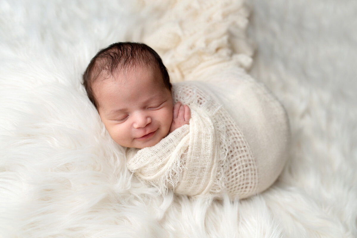 Newborn session of baby swaddled and smiling