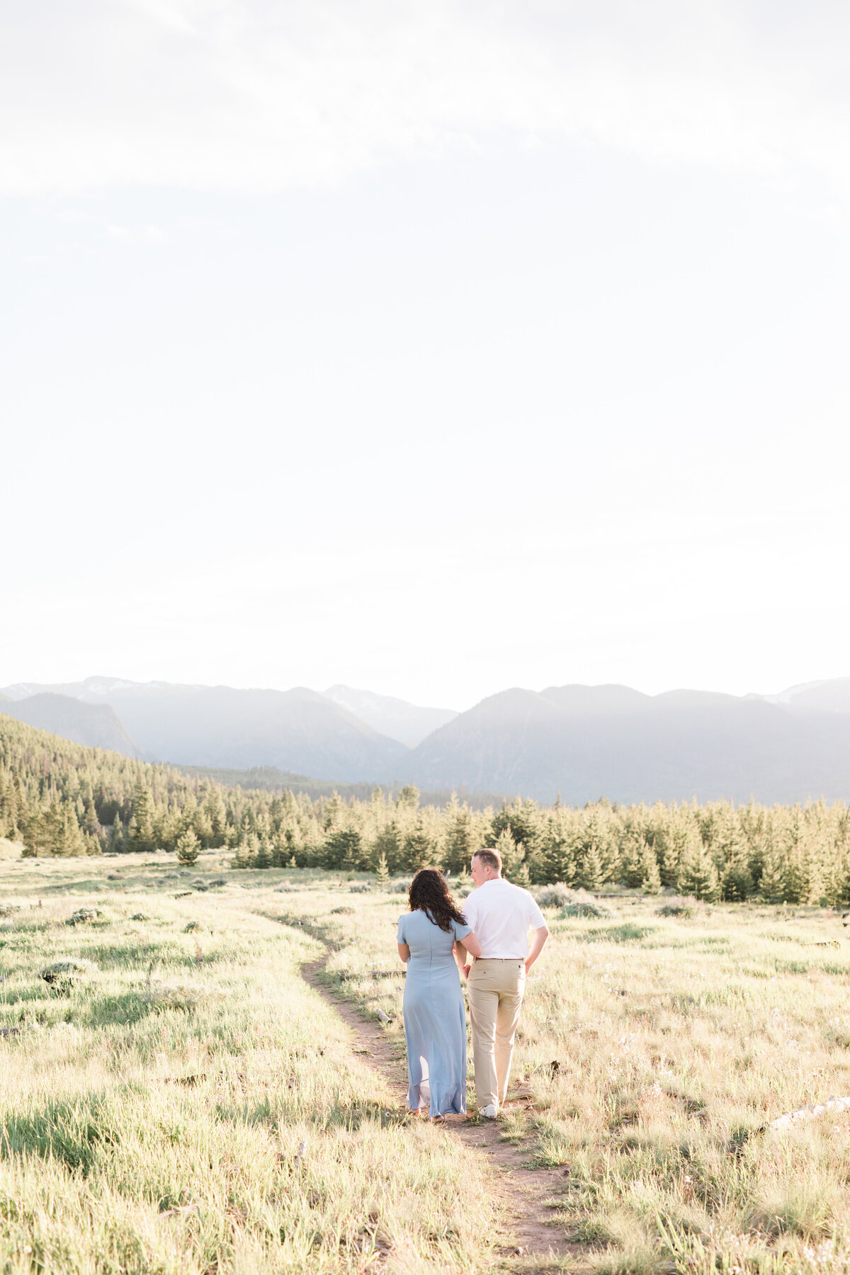 A couple is walking towards the sunset in a mountain field during the summer months