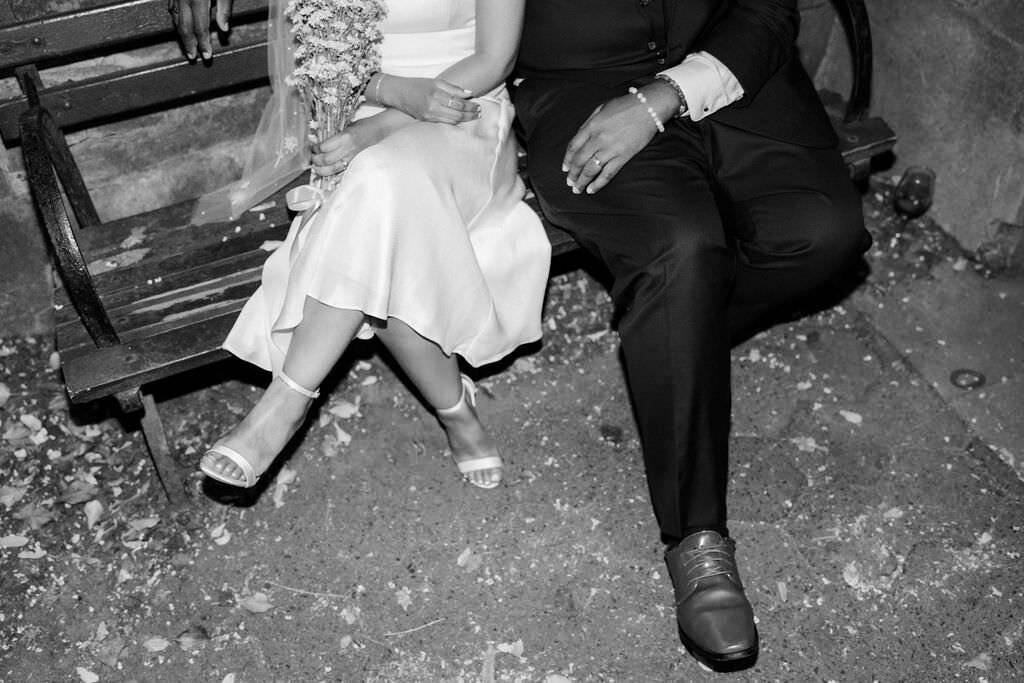 black and white photo of bride and groom's legs as they sit on a park bench