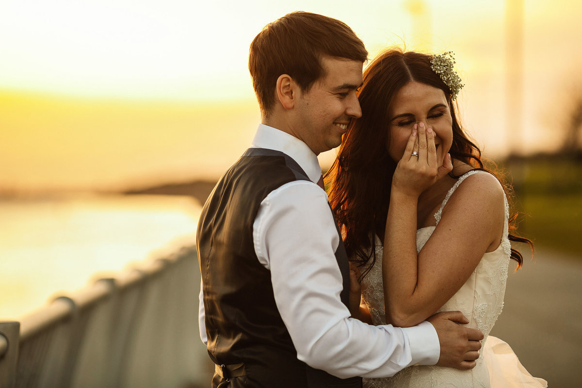A bride giggling as her husband tells a joke at sunset