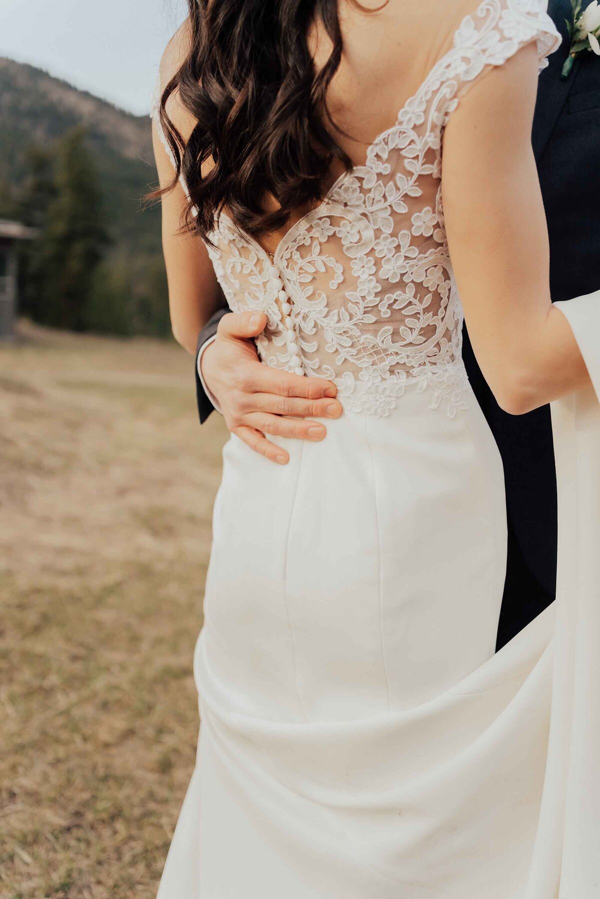 Maddie Rae Photography the back of the brides dress with the grooms hand wrapped around her waist as they dance. mountains in the background