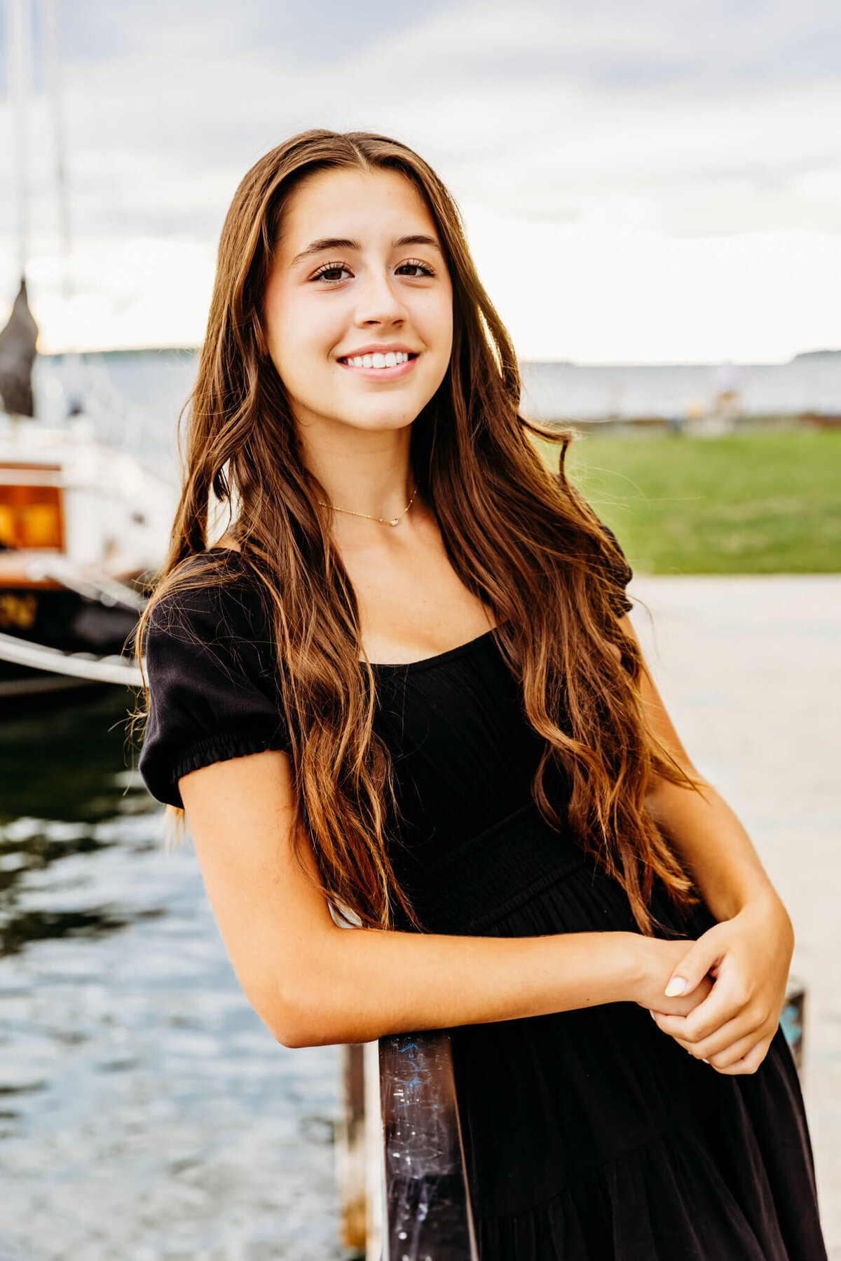 teen girl playing with hair and leaning on railing by sailboat during Green Bay senior photography session