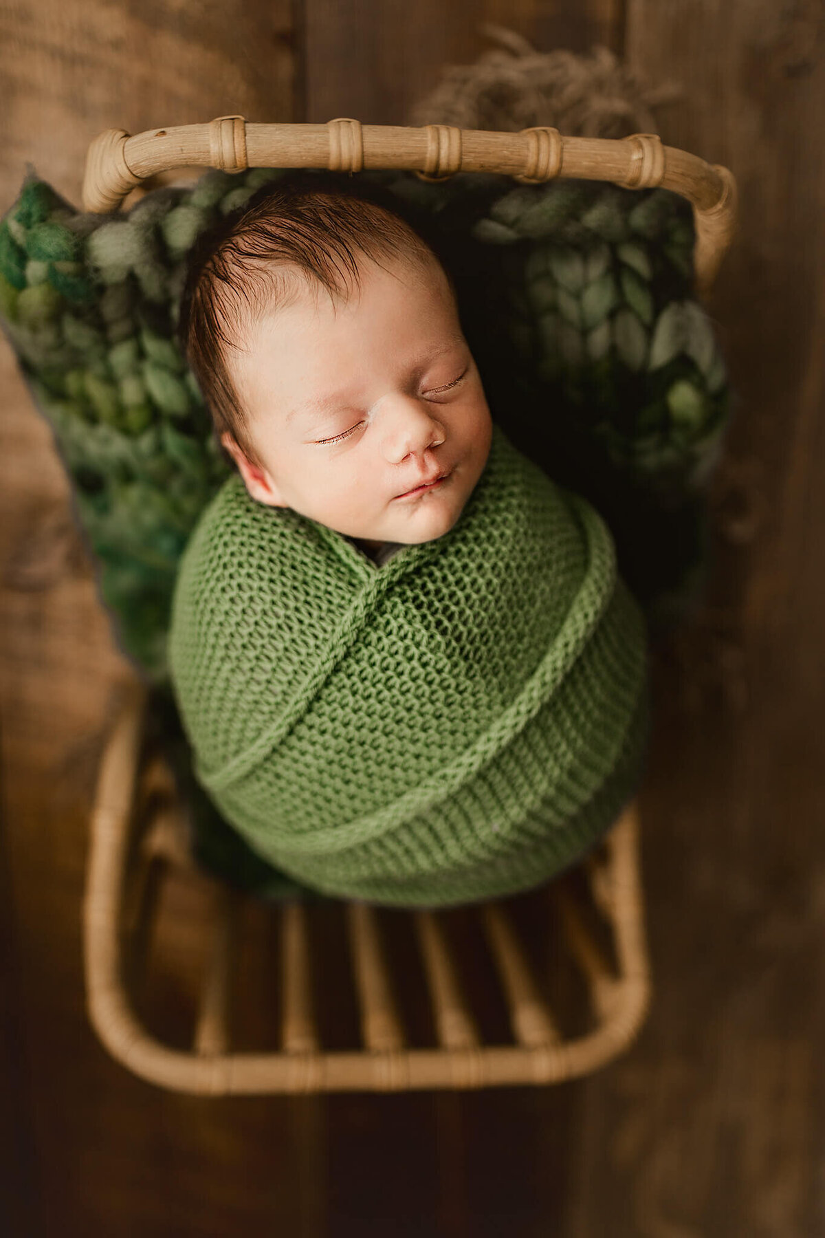 newborn baby boy swaddled in green + posed in bed prop