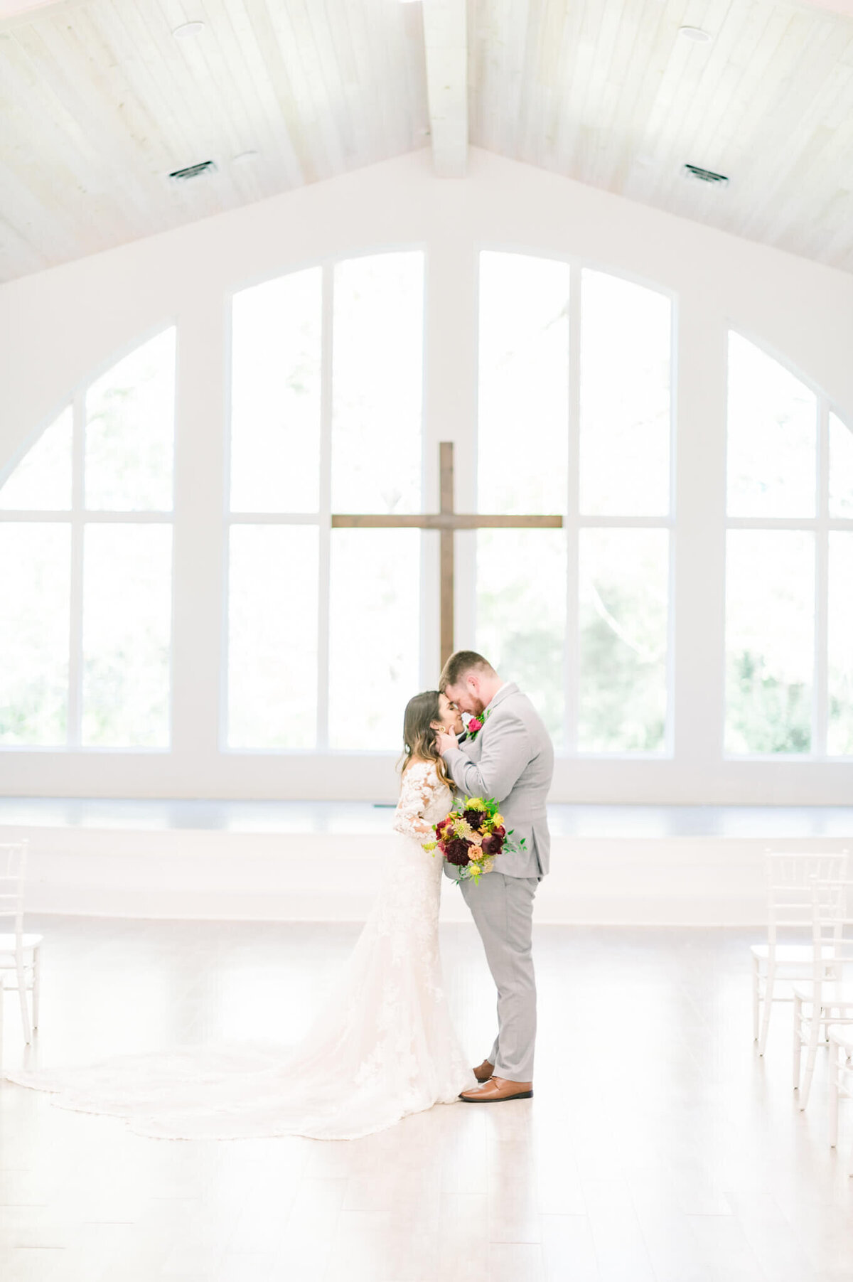 bride and groom rest their foreheads together in front of cross wedding arbor at arkansas wedding venue legacy acres, photo by em london photography, little rock wedding photographer