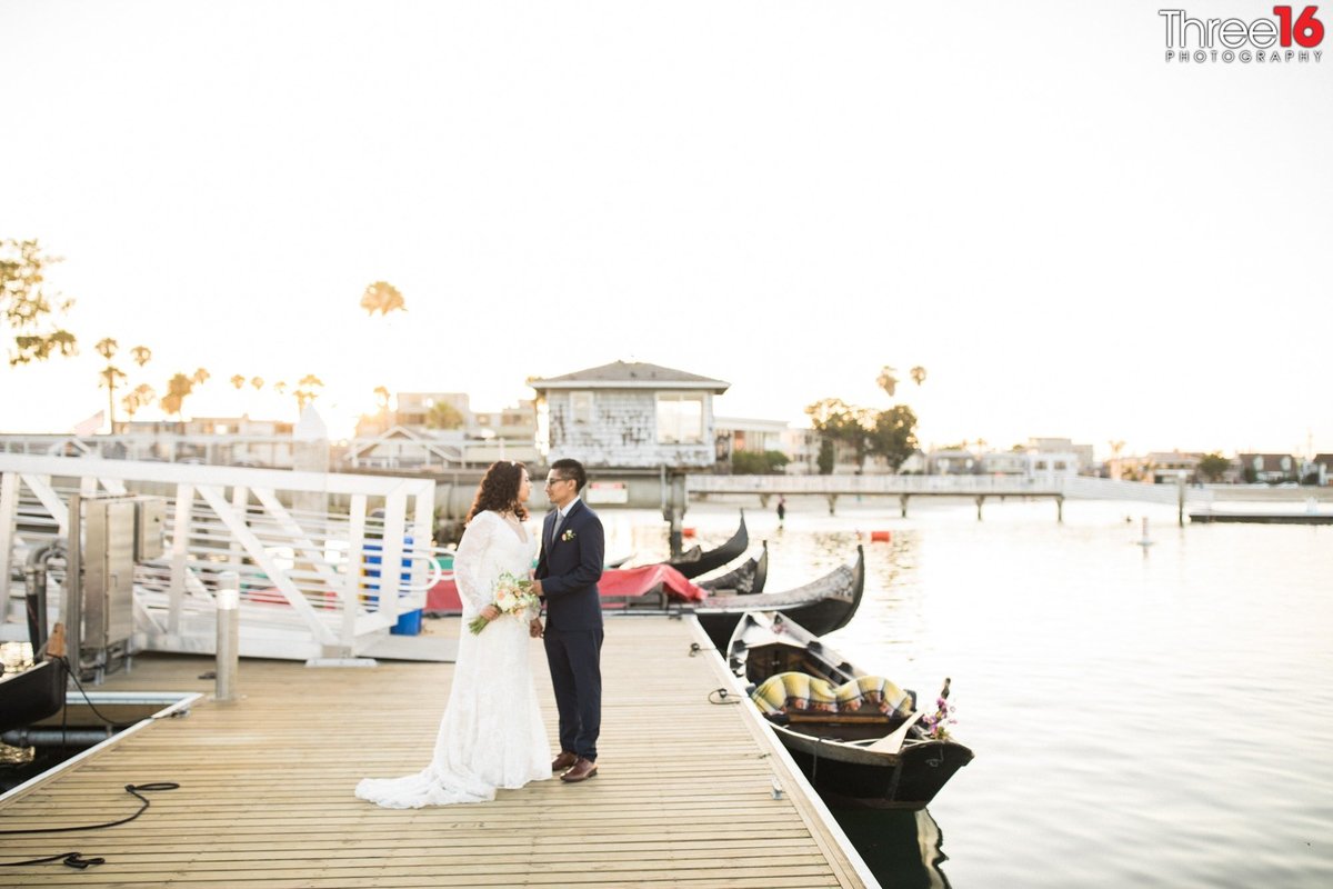Newly married couple look at each other during a photo shoot while standing on the dock
