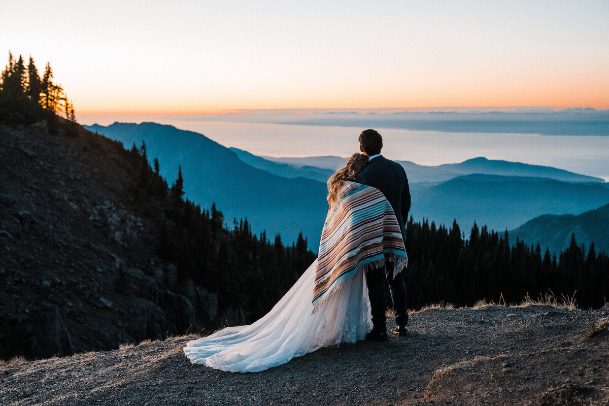 A bride and groom snuggle under a Pendleton blanket while enjoying the view on top of Hurricane Ridge after their Olympic National Park elopement