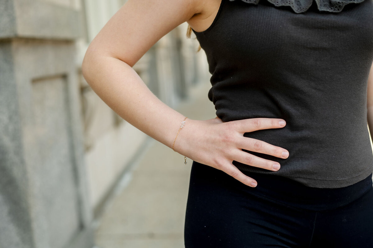 Woman with her hand on her lower back, indicating discomfort, standing against a blurred urban background.