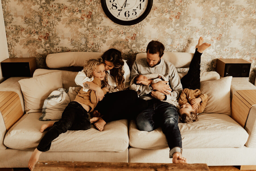 familj med nyfödd bebis och två syskon sitter i soffa under lifestylefotografering i halmstad