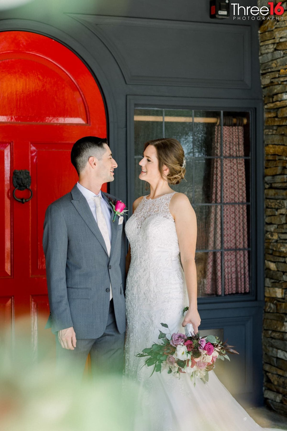 Bride and Groom stop to look at each other in front of the red door entrance to the Summit House Restaurant