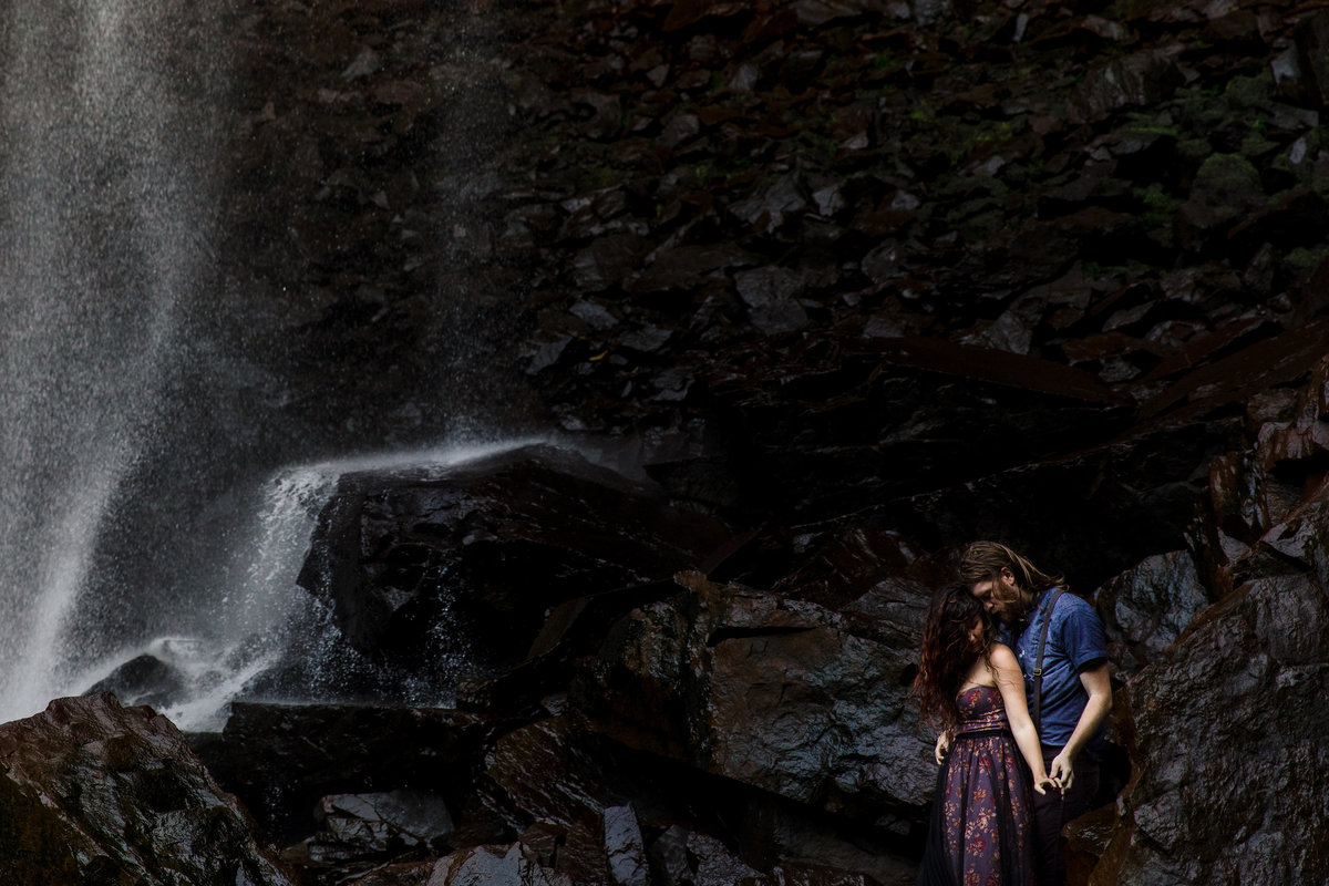 The couple hold each other with a waterfall backdrop in Maine