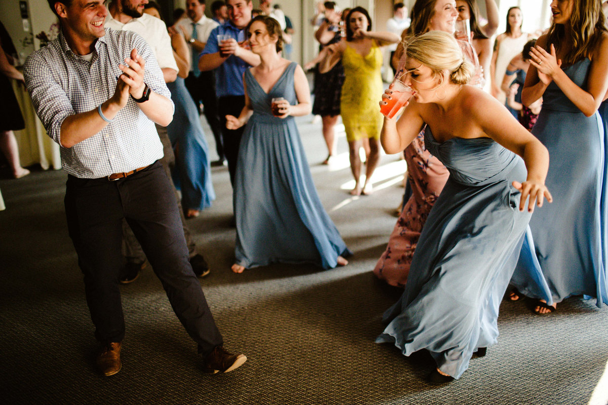 bridesmaid dances while taking a drink on dancefloor with dress blowing in wind