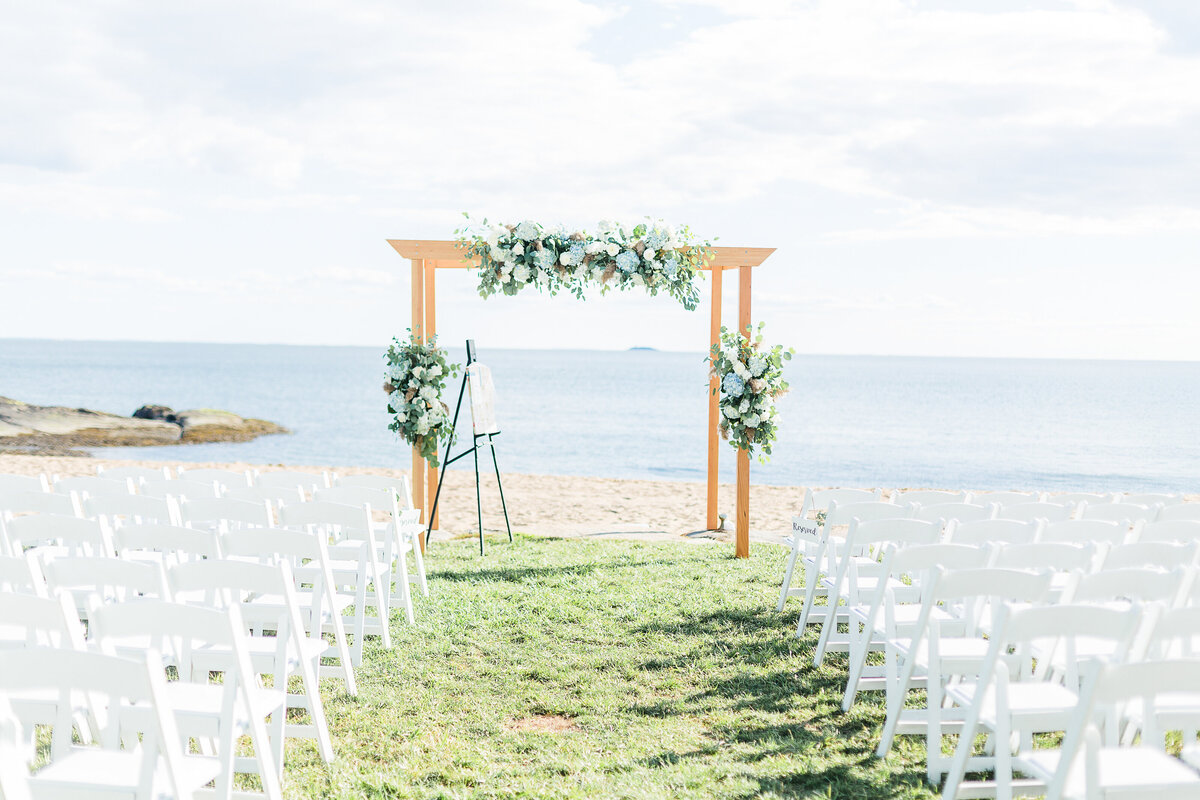 Detail image of the oceanside wedding ceremony location at the Madison beach hotel. White wood chairs, a wooden flower-adorned arch.
